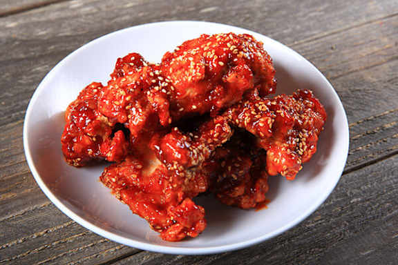 A plate of chicken wings covered in a red sauce and sesame seeds.