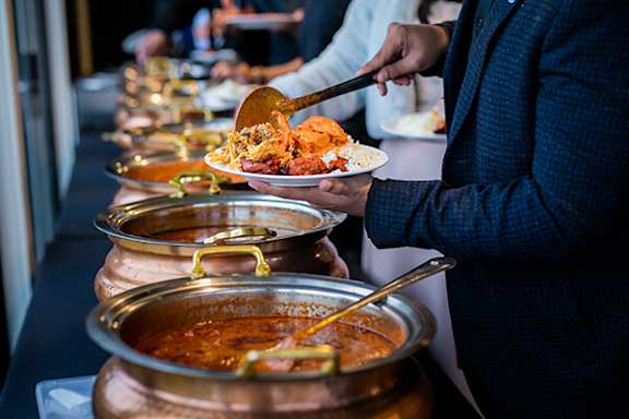 A person is serving food from a large pot into a smaller pot.