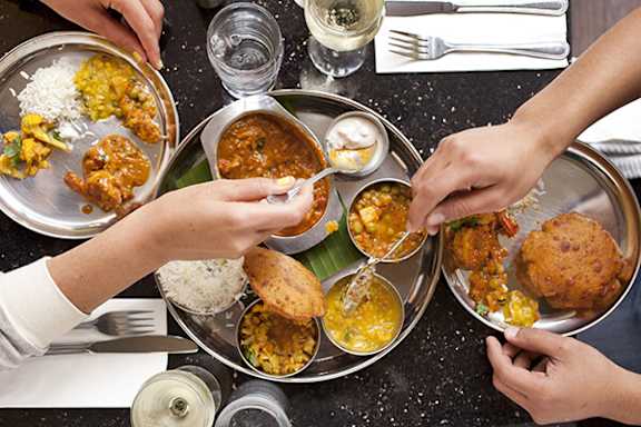 A group of people are serving themselves food from a large metal platter.