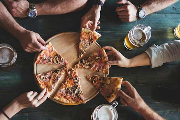 A group of people sharing a pizza and beer.