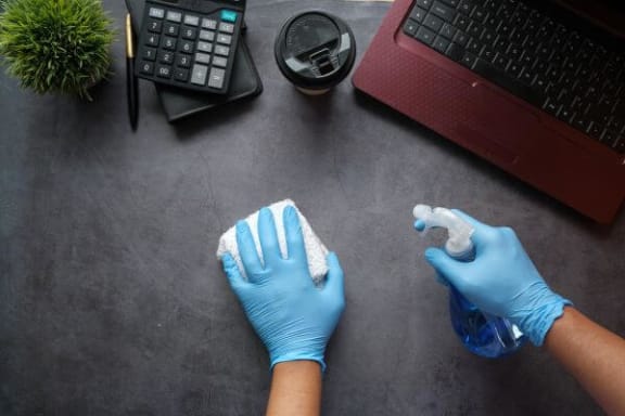 a person in blue gloves is wiping a laptop