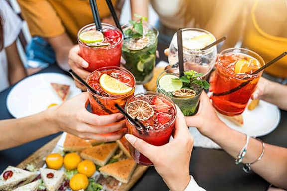 A group of people toasting with colorful cocktails.