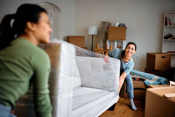 Two women unpacking in a room with boxes and furniture.