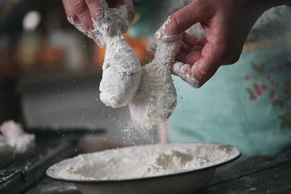 A person is sprinkling flour onto dough in a bowl.