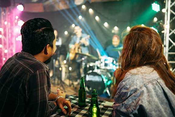 A man and a woman are sitting at a table, facing a stage with a band performing on it.