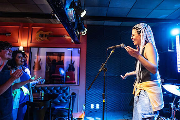 A woman with dreadlocks is singing into a microphone in a dimly lit room.