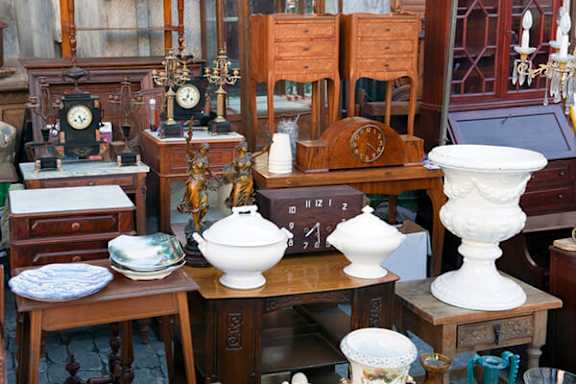 A collection of antique items including clocks, bowls, and vases are displayed on wooden tables.