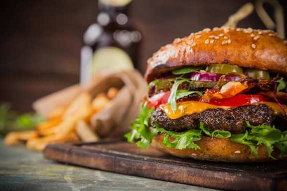 A burger with lettuce, tomato, and pickles on a sesame seed bun.