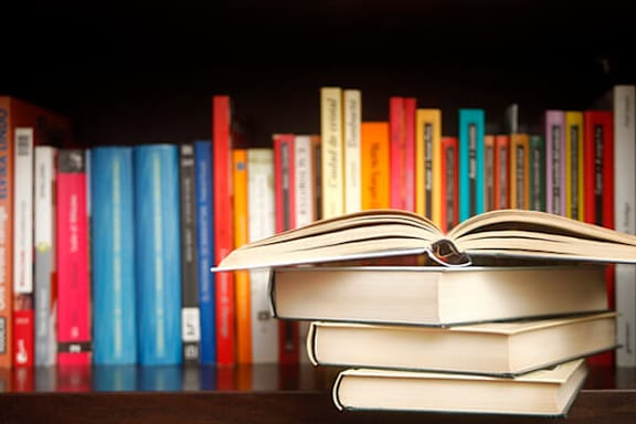 A stack of books with one open on a shelf.