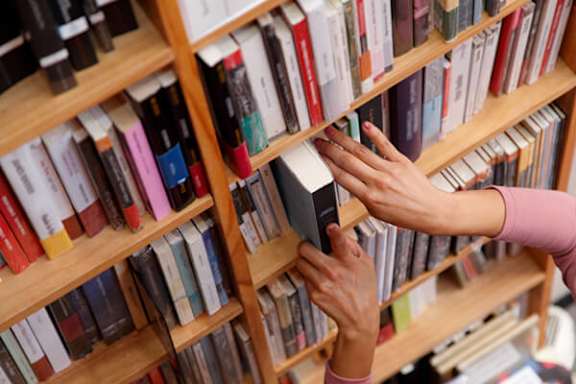 A person is reaching for a book on a shelf.