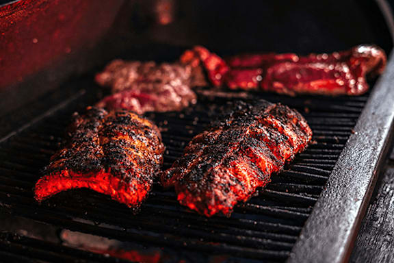 Meat cooking on a grill with a dark background.