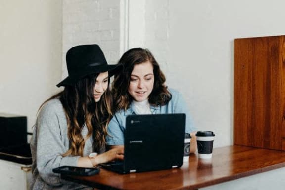 two women sitting at a table looking at a laptop