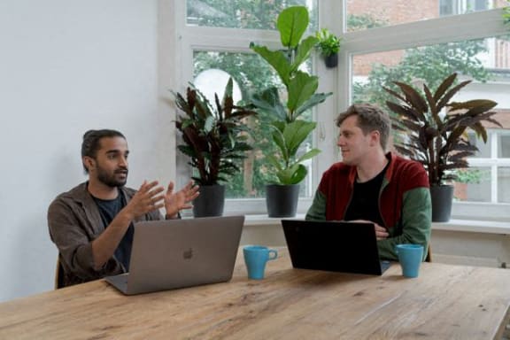 two men sitting at a table with laptops