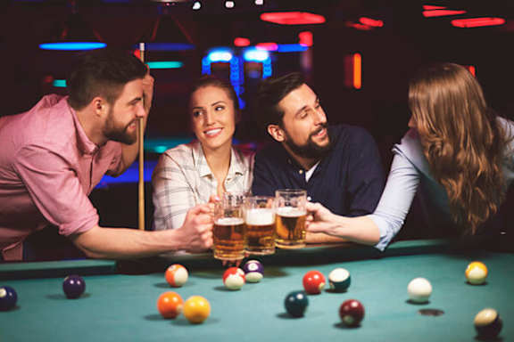 Three people are playing pool and drinking beer.