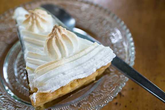 A slice of lemon meringue pie on a glass plate with a pie server.