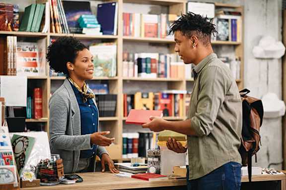 A man is handing a book to a woman in a bookstore.