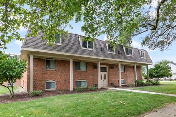 the front of a brick house with a lawn and trees