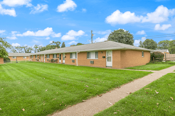 a long brick building with a grass yard and a sidewalk
