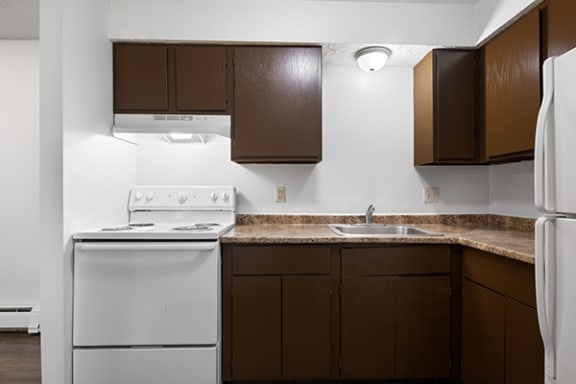 an empty kitchen with white appliances and brown cabinets