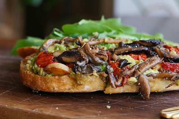 A mushroom and tomato topped bruschetta on a wooden board.