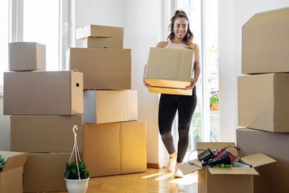A woman is carrying a box while surrounded by a large number of other boxes.