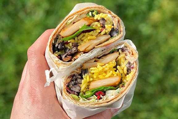 A person is holding a wrap with rice, beans, and vegetables.