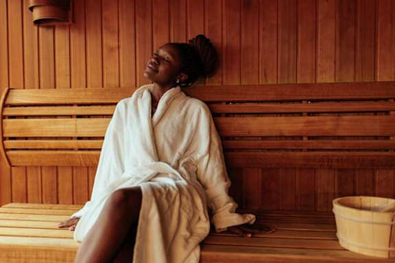 A woman in a white robe is sitting in a wooden sauna.