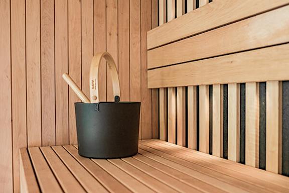 A bucket with a wooden handle sits on a wooden bench in a sauna.