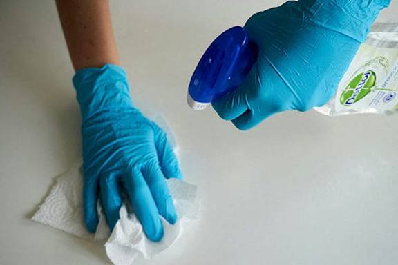 A person wearing blue gloves is cleaning a surface with a white cloth.