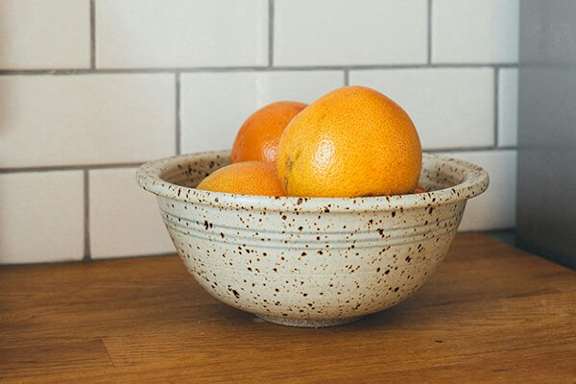 Two oranges in a speckled bowl on a wooden table.