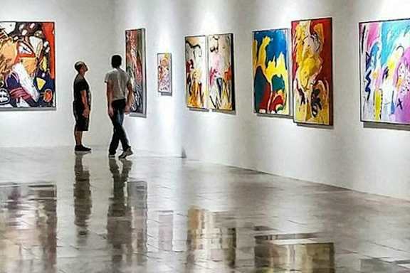 Two people are looking at paintings in an art gallery.