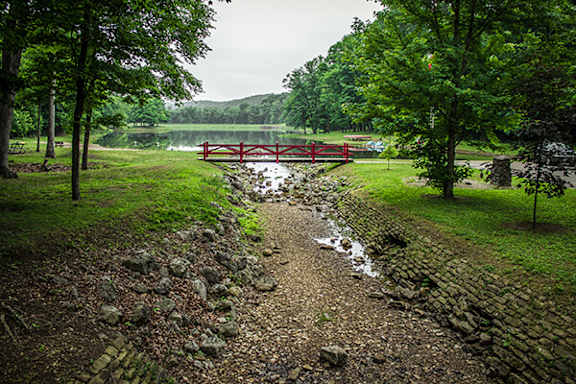 A red bridge crosses a stream in a green landscape.