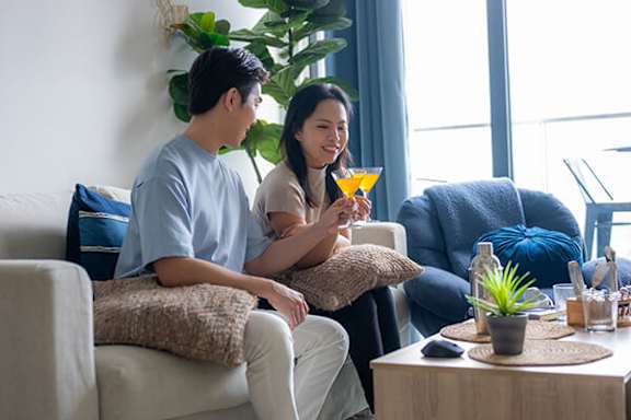 A man and a woman are sitting on a couch with a drink in hand.