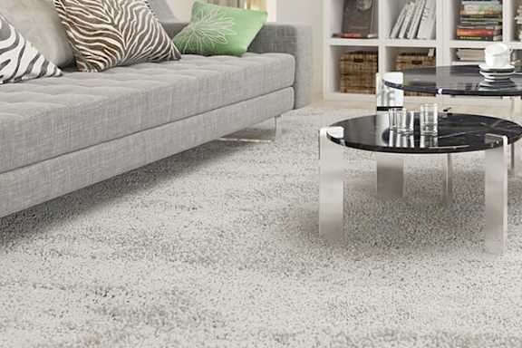 A grey couch with a glass table in front of it.