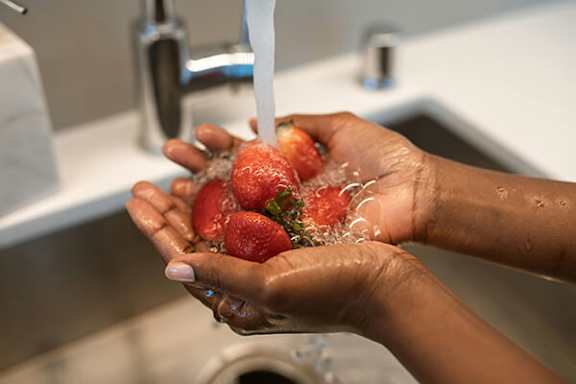 A person washing strawberries under running water.