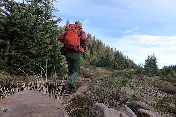 A man with a red backpack is hiking on a rocky trail.