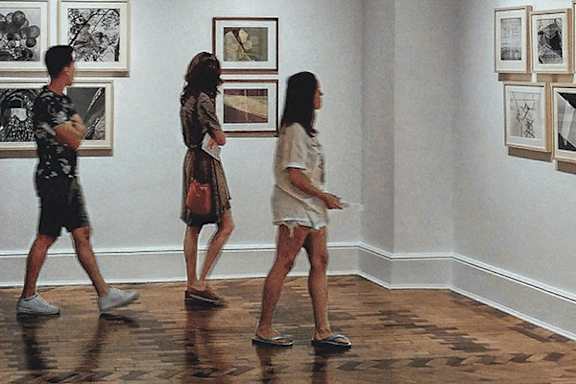 a group of people walking through an exhibition of paintings