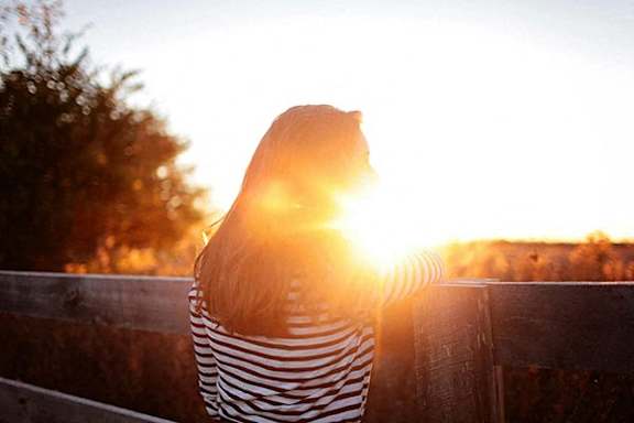 a woman is looking over a fence at the sun