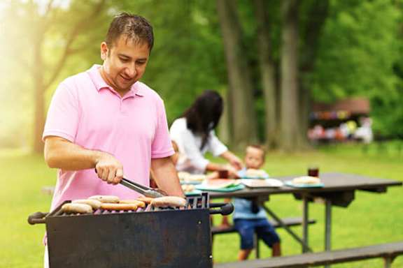 A man in a pink shirt is grilling food on a barbecue.