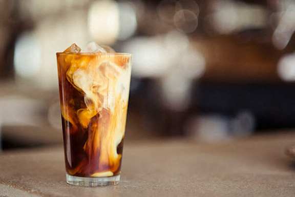 A glass of iced coffee with ice cubes on a table.