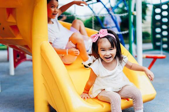 Two children playing on a slide in a playground.