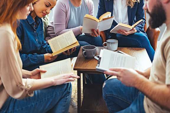 A group of people sitting together, each reading a book.