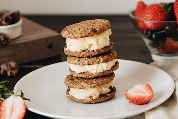 A stack of cookies with cream filling and a strawberry on a white plate.