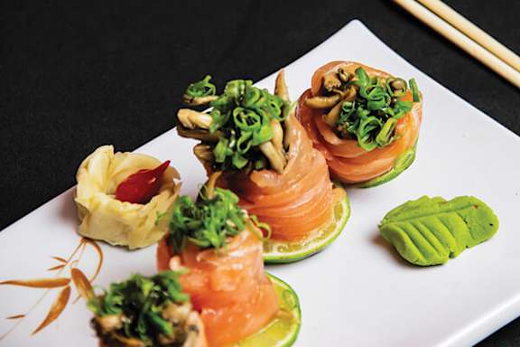 A plate of sushi with salmon, avocado, and green onions.