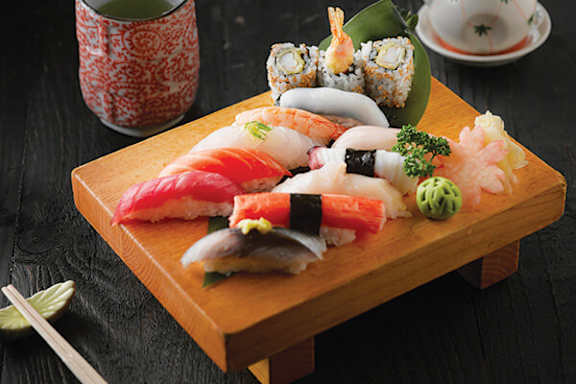 A wooden board with sushi and chopsticks on a black background.