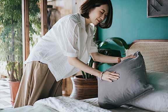 A woman is arranging a pillow on a bed.