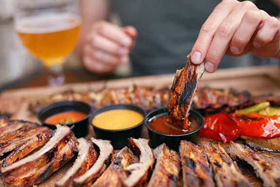 A person is cutting a piece of meat from a platter of barbecued meats.