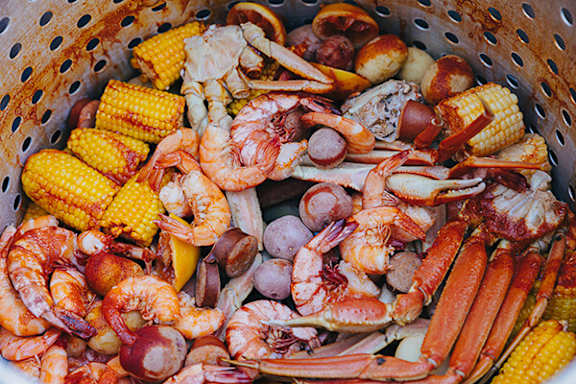 A variety of seafood and corn in a colander.