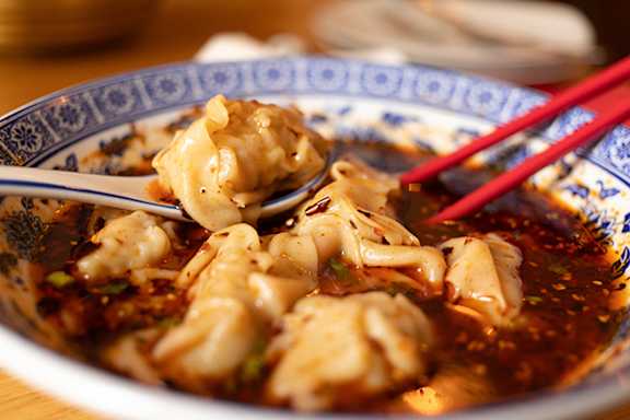 A bowl of dumplings with a pair of red chopsticks.