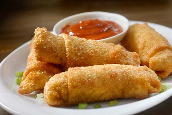 A plate of fried spring rolls with a side of dipping sauce.